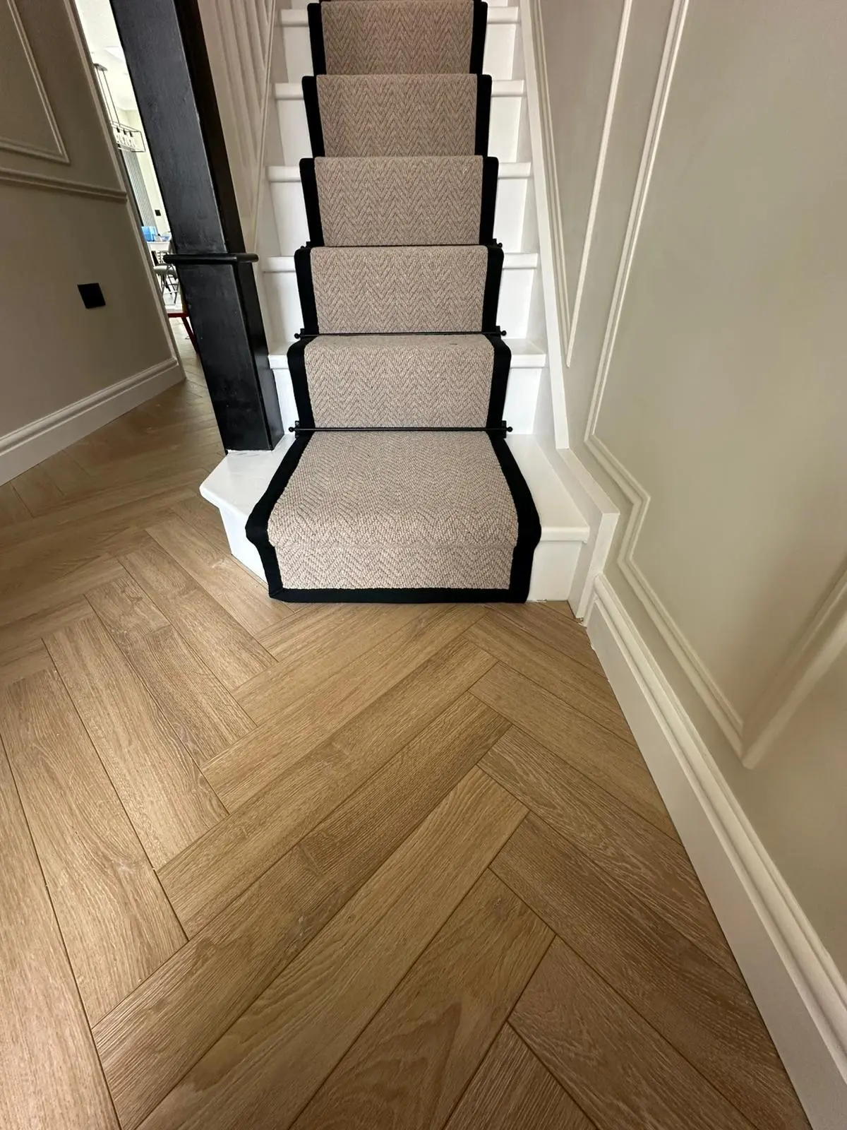 Natural oak herringbone parquet flooring in a hallway with a bordered stair runner
