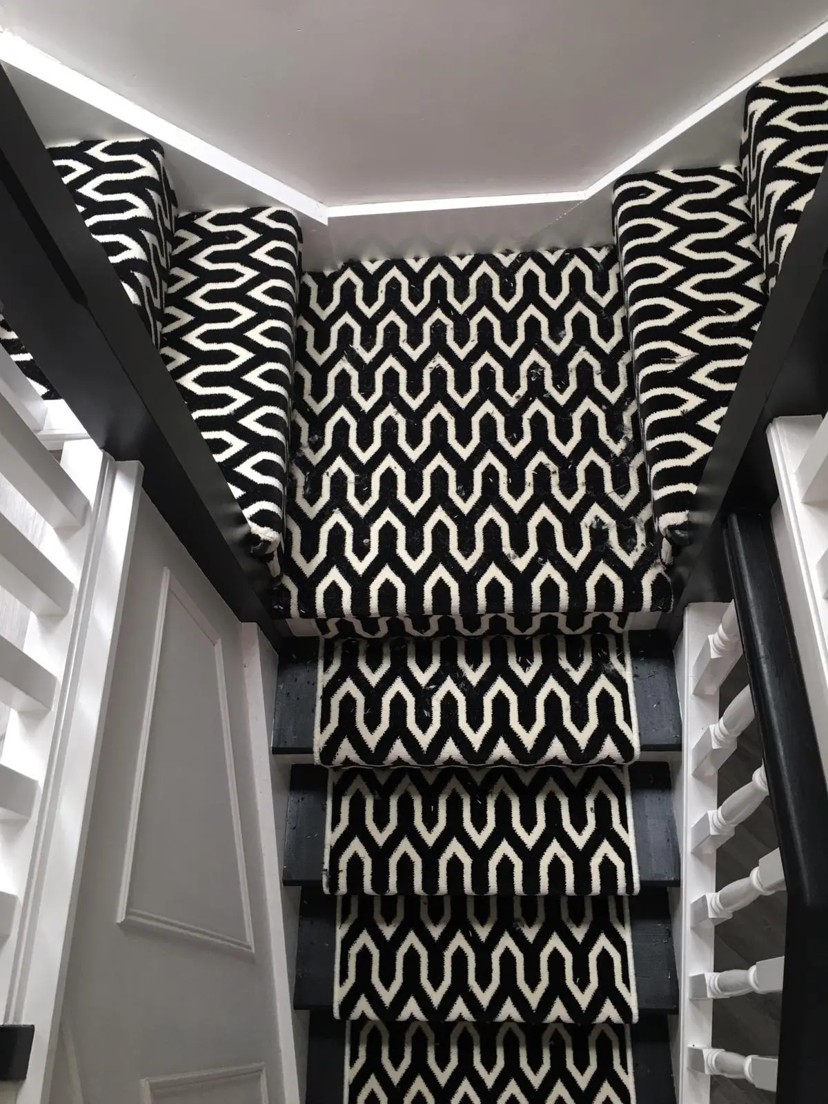 Black and cream geometric patterned stair runner on black-painted stairs with white spindles